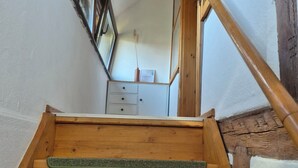 Una escalera de madera con alfombra verde que conduce a una habitación con un aparador blanco y una planta pequeña.