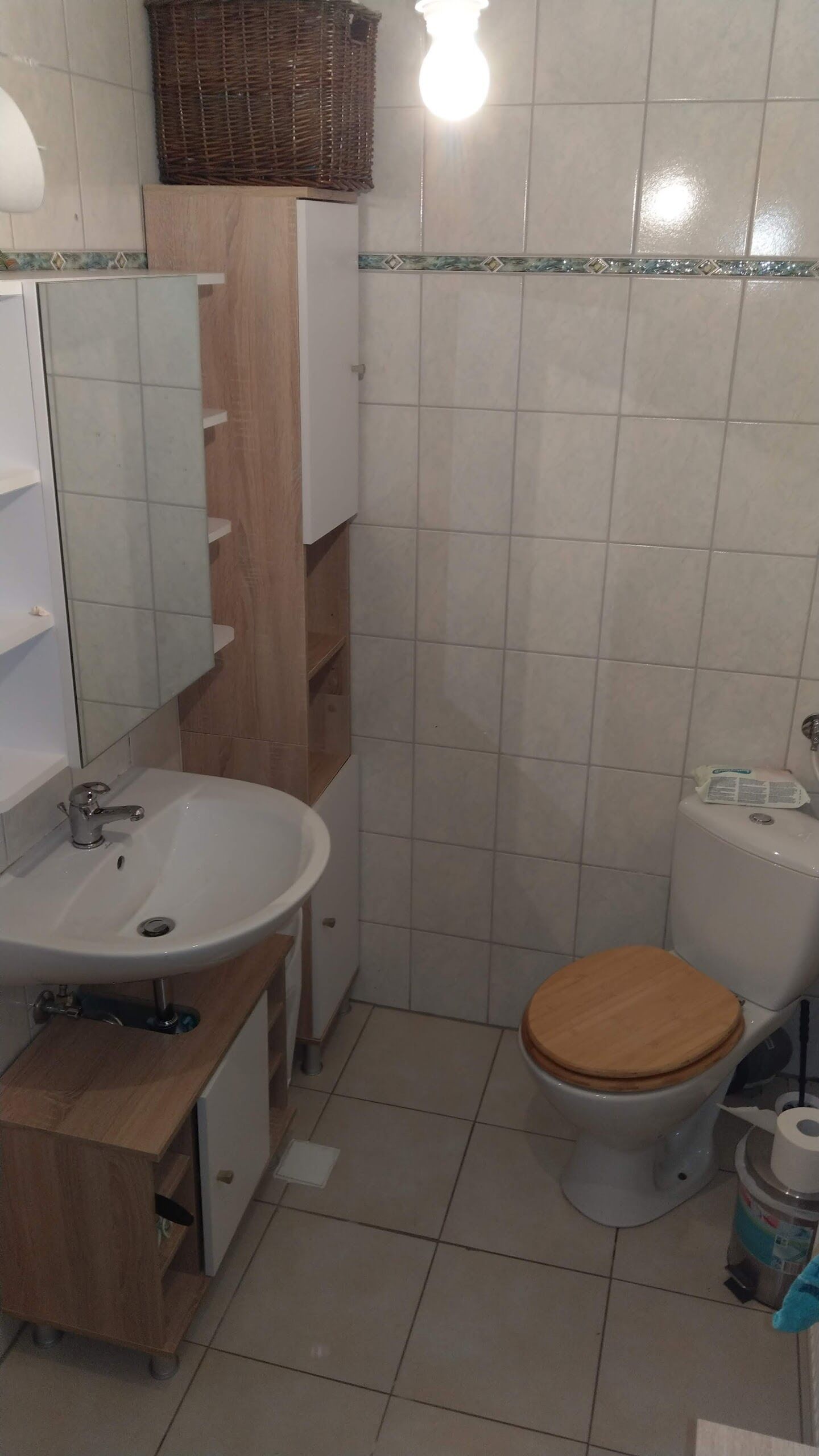 Een badkamer met een witte wastafel, een houten kastje en een toilet met een houten zitje.