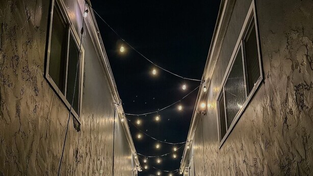 Un couloir étroit, illuminé de guirlandes lumineuses, bordé de murs percés de fenêtres et doté d’un sol en béton.