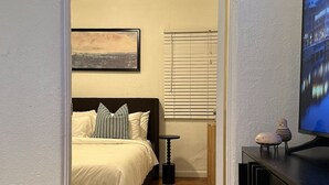 Une chambre à coucher comprenant un lit, une table de chevet, un téléviseur et une fenêtre avec des stores.