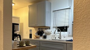 Une cuisine moderne avec des meubles gris, un four encastré, un évier et une fenêtre équipée de stores.
