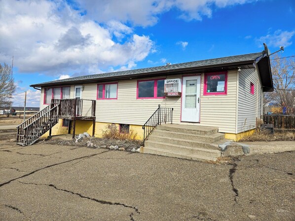 A small, single-story motel with a white exterior and pink trim. It has a front entrance with a door marked "OPEN" and a sign indicating a vacancy. - GULL LAKE LODGE MOTEL (Gull Lake)