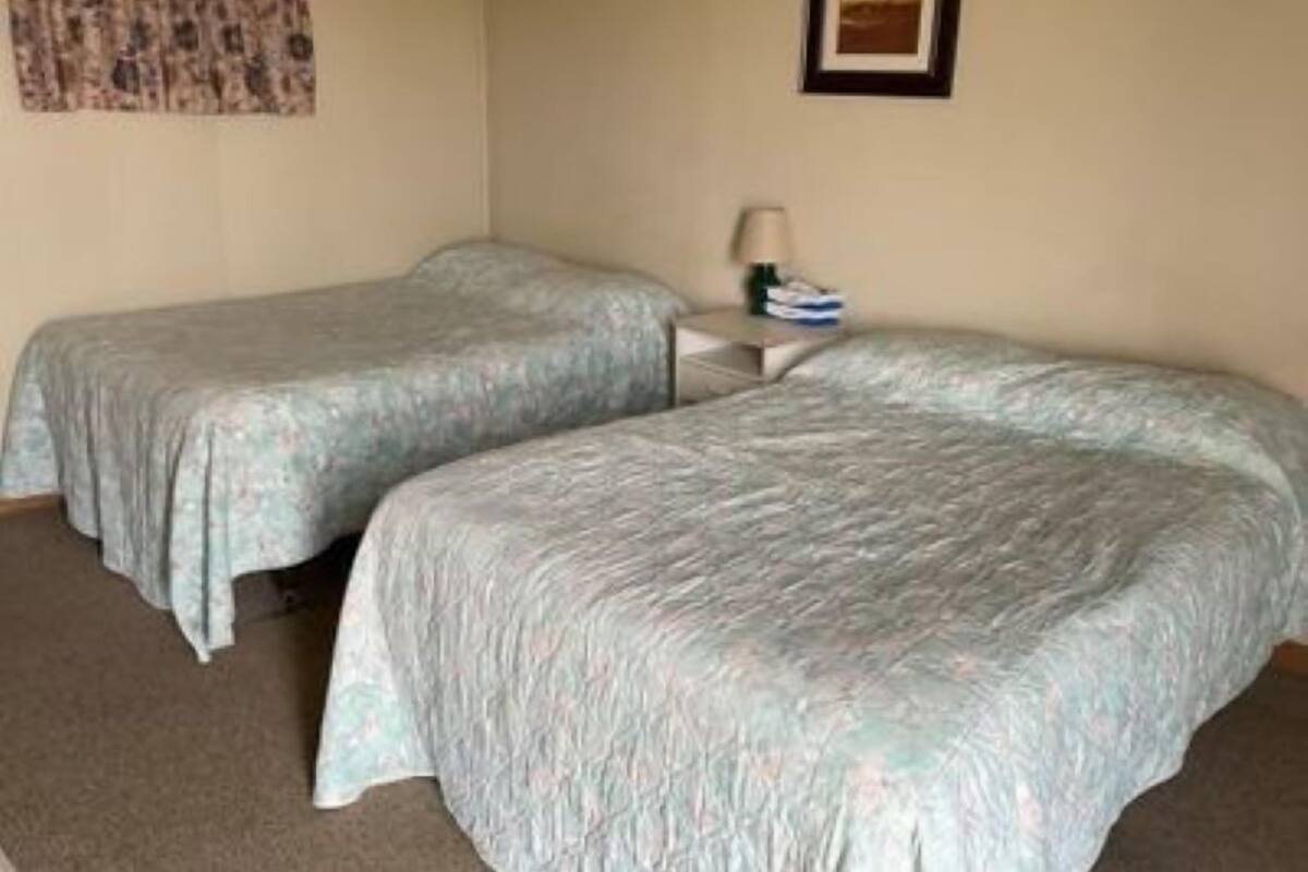 A room with two single beds, a small bedside table with a lamp, and a framed picture on the wall.