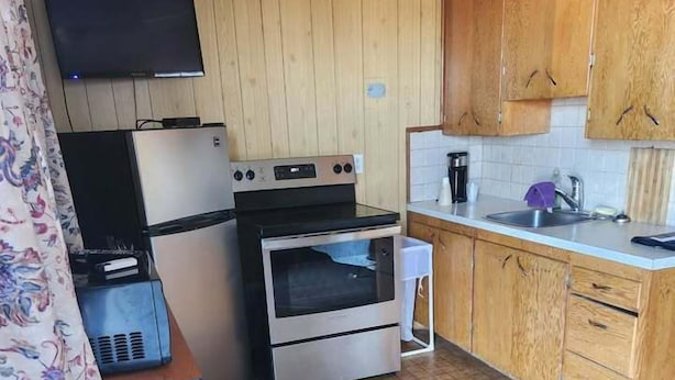 A compact kitchen with wooden cabinets, a built-in oven, a microwave, and a small sink. - GULL LAKE LODGE MOTEL (Gull Lake)