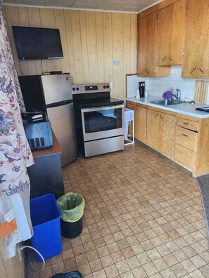 A compact kitchen with wooden cabinets, a built-in oven, a microwave, and a small sink. - GULL LAKE LODGE MOTEL (Gull Lake)
