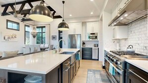 Een moderne keuken met een groot eiland, roestvrijstalen apparatuur en hanglampen.