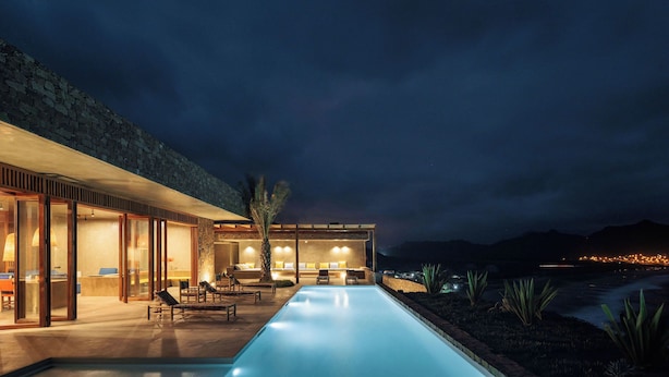Un hotel moderno con piscina, mobiliario exterior y vistas a las montañas.