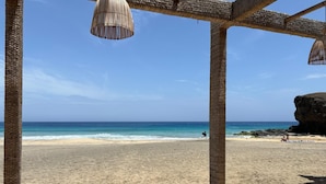 Una playa con una estructura de techo de paja, sillas de madera y vista al océano.