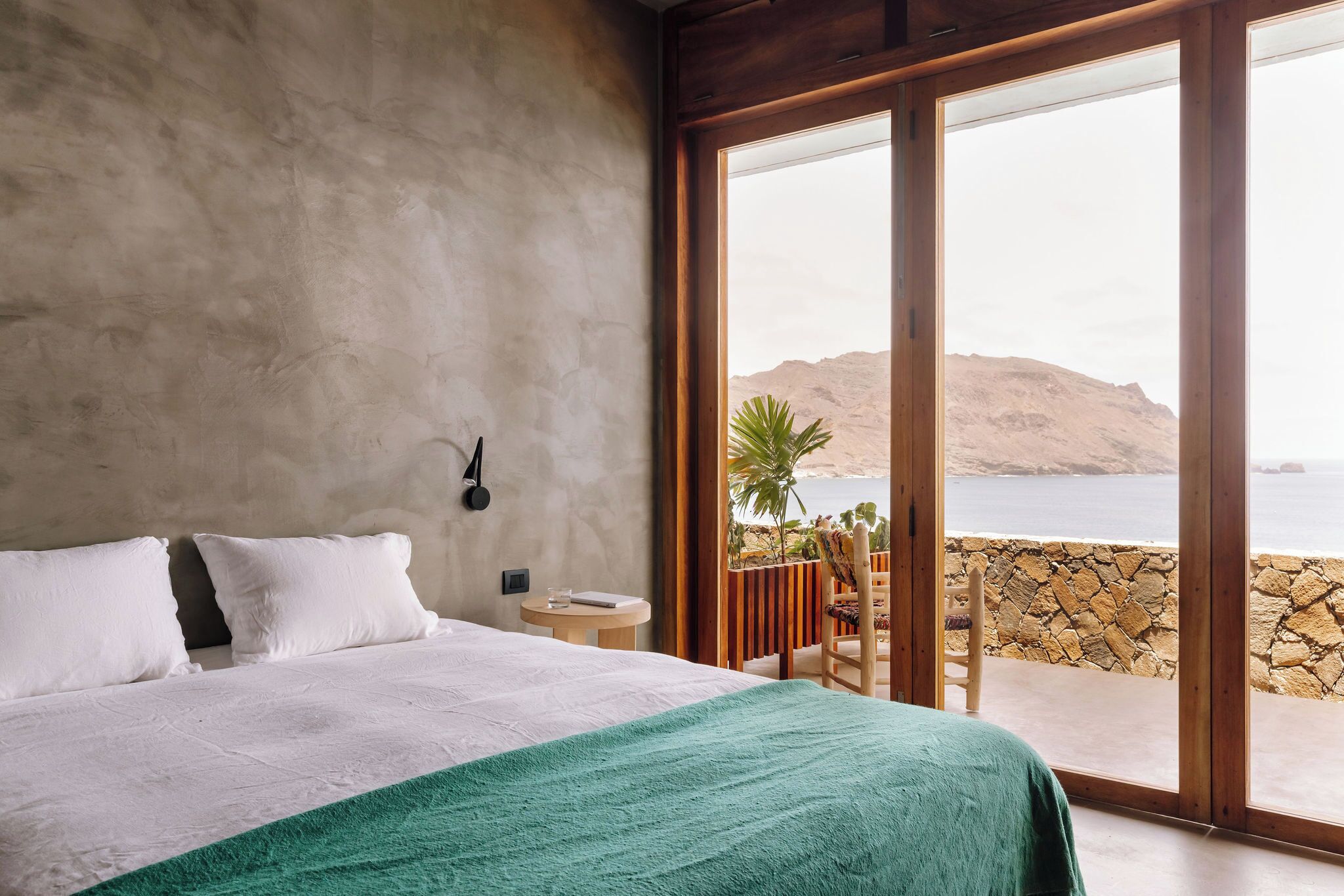 A bedroom with a large bed, a small table, and a view of the sea through a glass door.