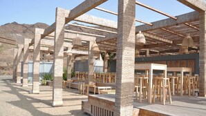 Un espacio al aire libre con mesas y sillas de madera, pilares de piedra y lámparas colgantes.