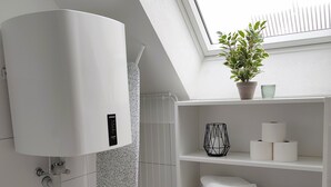 A modern bathroom with a skylight, a white radiator, a step stool, a shelf with towels and toiletries, and a potted plant.