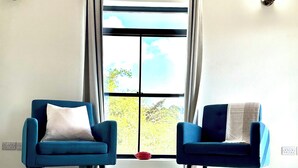 Ein Zimmer mit zwei blauen Sesseln, einem gemusterten Teppich und einem Fenster mit Vorhängen.