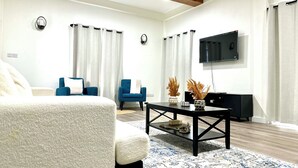 Ein modernes Wohnzimmer mit einer Couch, einem blauen Sessel, einem Couchtisch mit Dekoration, einem Flachbildfernseher und einer Holzzahl.