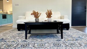 Ein Wohnzimmer mit einem weißen Sofa, einem schwarzen Couchtisch und zwei Vasen mit getrockneten Pflanzen.