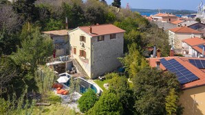 A stone building with a red-tiled roof, a swimming pool, and solar panels.