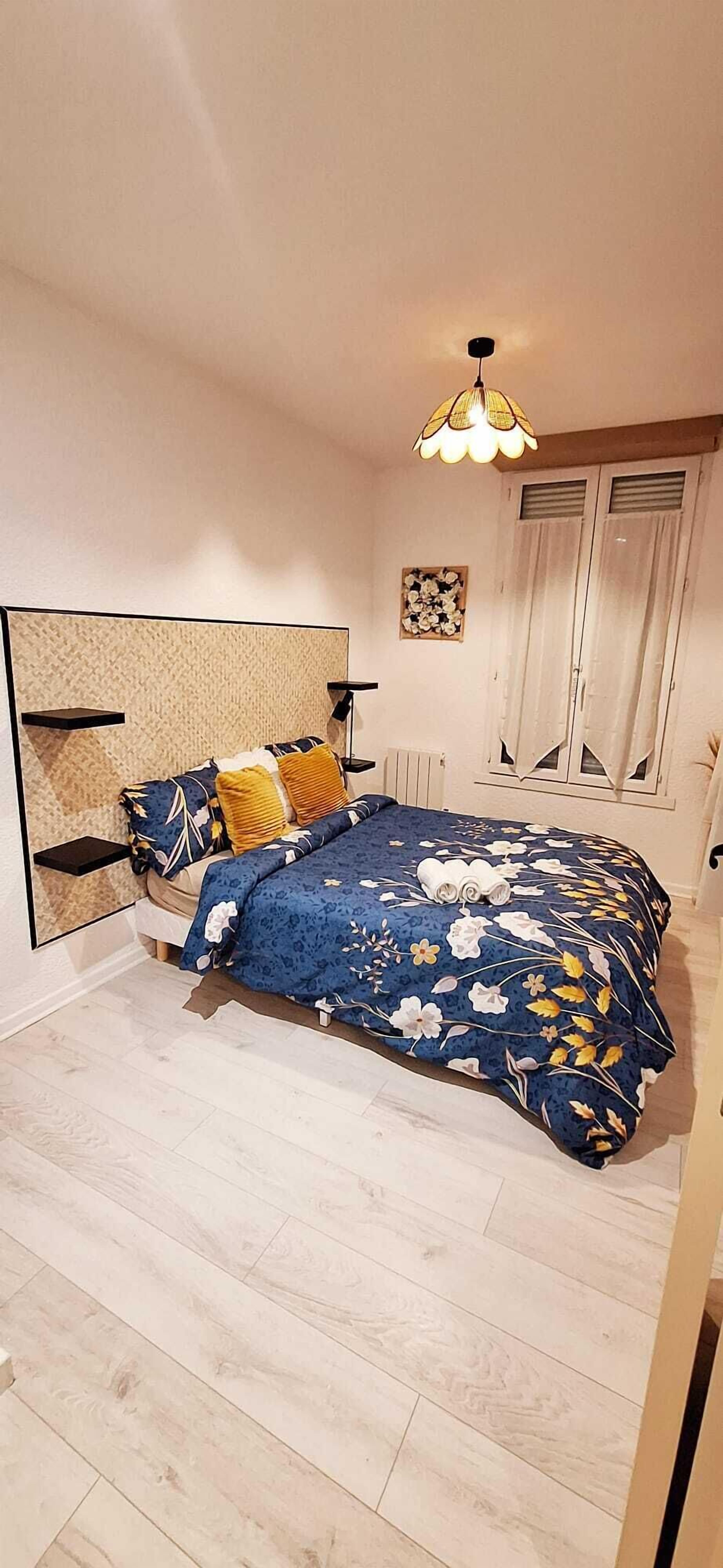 Une chambre à coucher avec un lit, une table de chevet, une lampe, un radiateur et une fenêtre avec des rideaux.