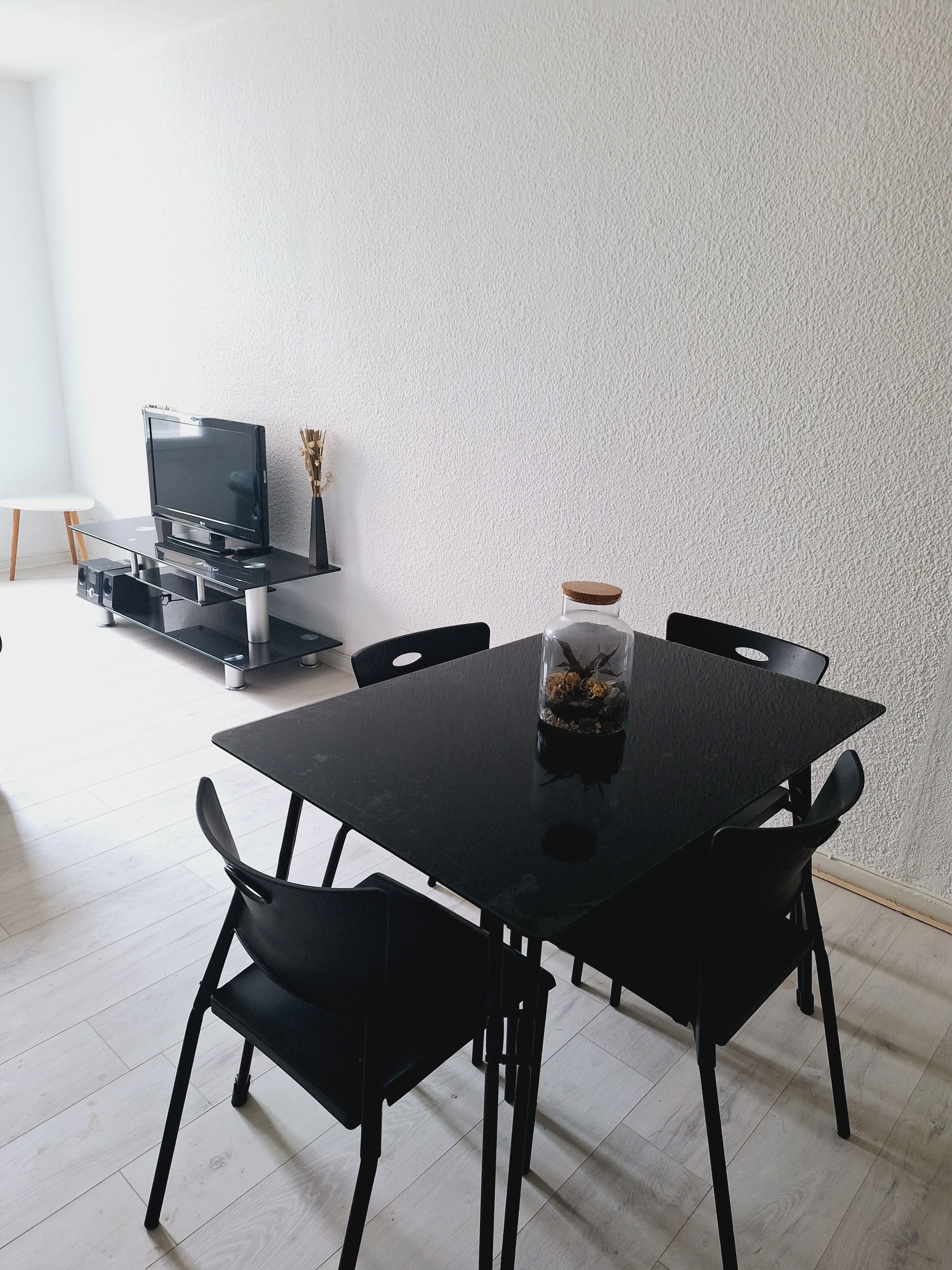 Een eetgedeelte met een zwarte tafel en stoelen, een televisie op een standaard, en een decoratieve vaas op de tafel.