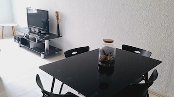 Een eetgedeelte met een zwarte tafel en stoelen, een televisie op een standaard, en een decoratieve vaas op de tafel.