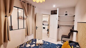 A bedroom with a bed, a chair, a wardrobe, and a door leading to a kitchen. - Attractive, renovated 2-room apartment by the lake (Saint-Jean-d'Angély)