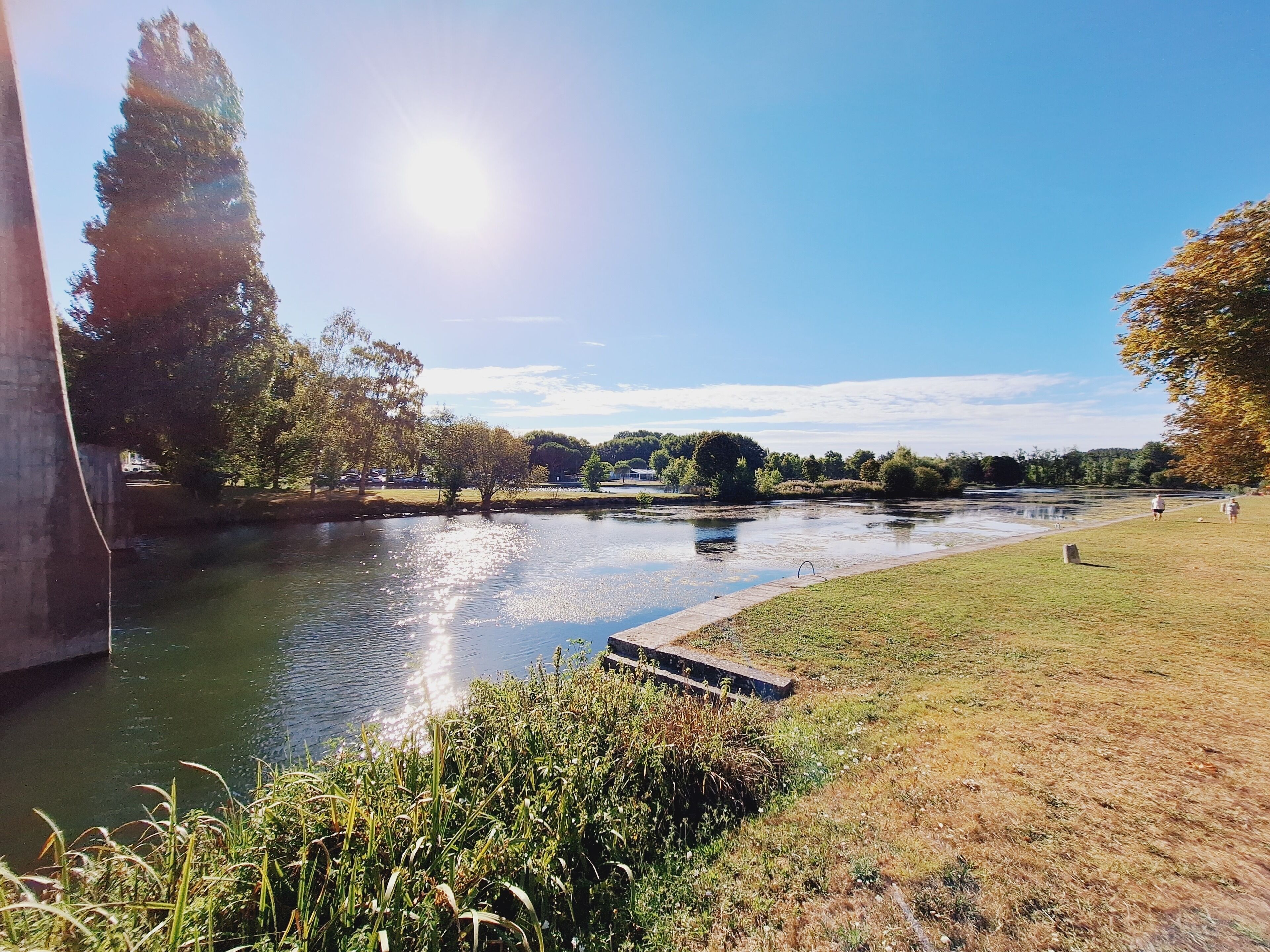 A riverside park with a walking path, trees, and a grassy area.
