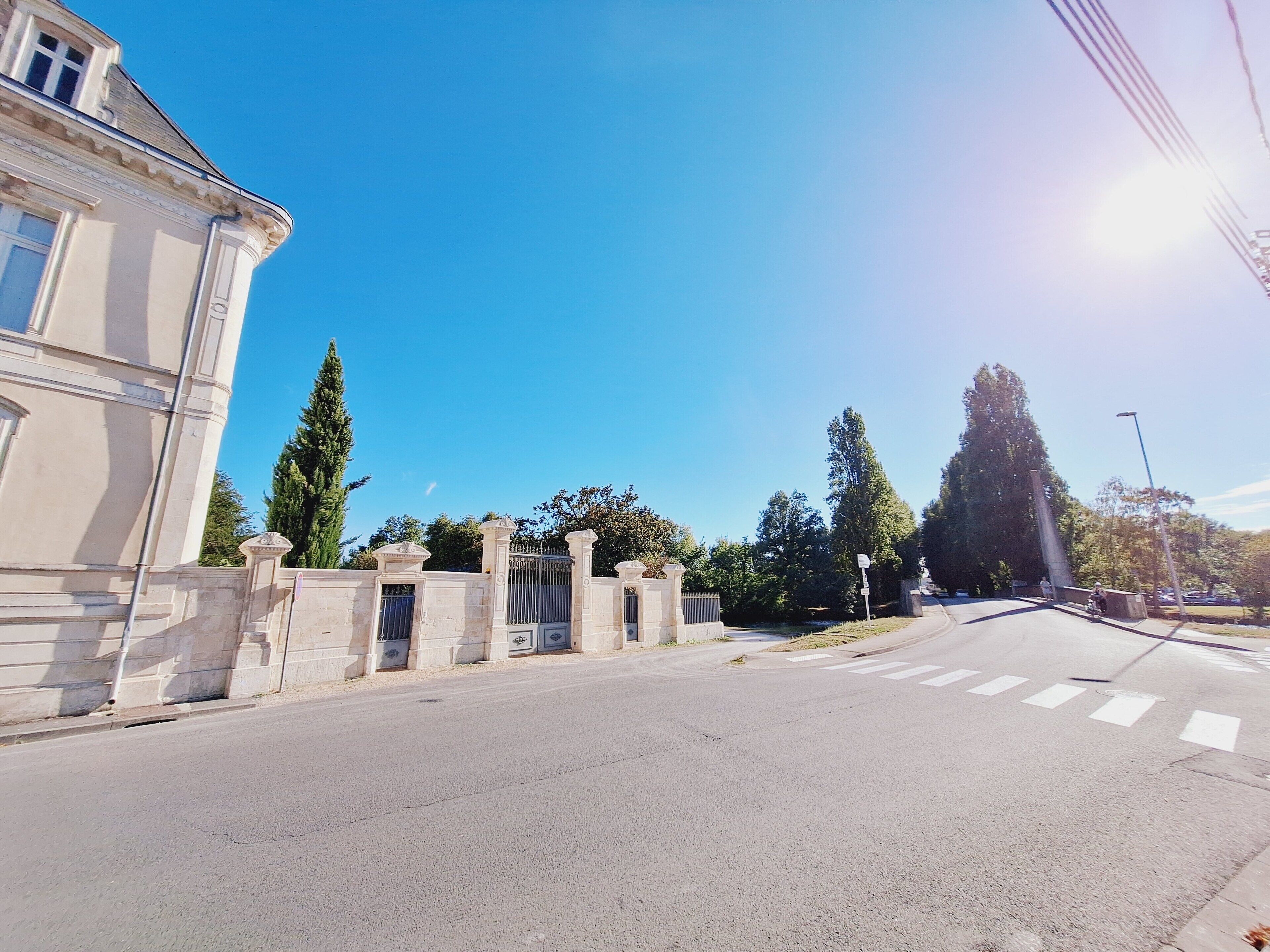 Une large route, déserte, avec une entrée fermée par un portail menant à un bâtiment situé sur la gauche.