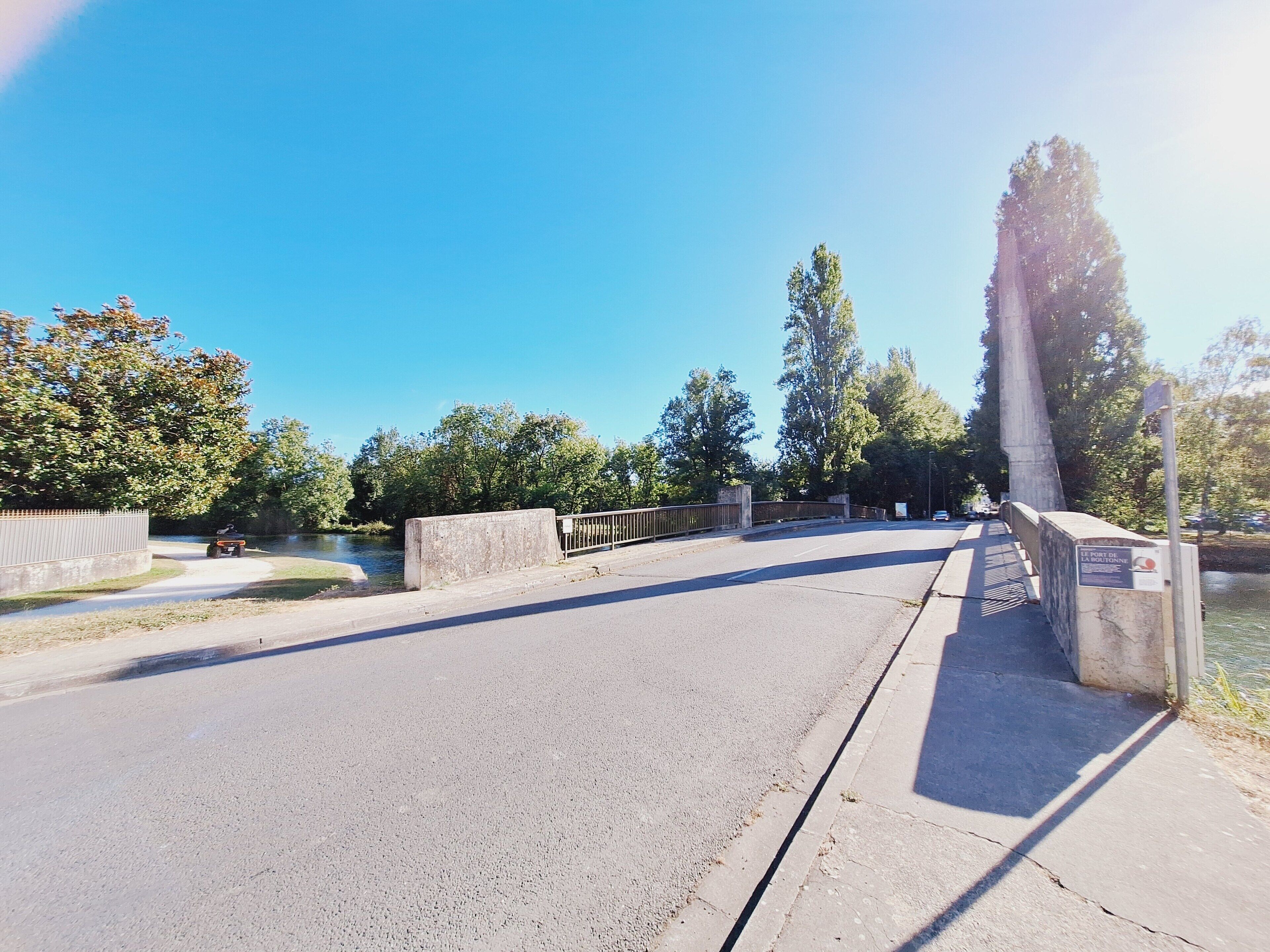 A bridge with a metal railing, a clear sky, and trees in the background.