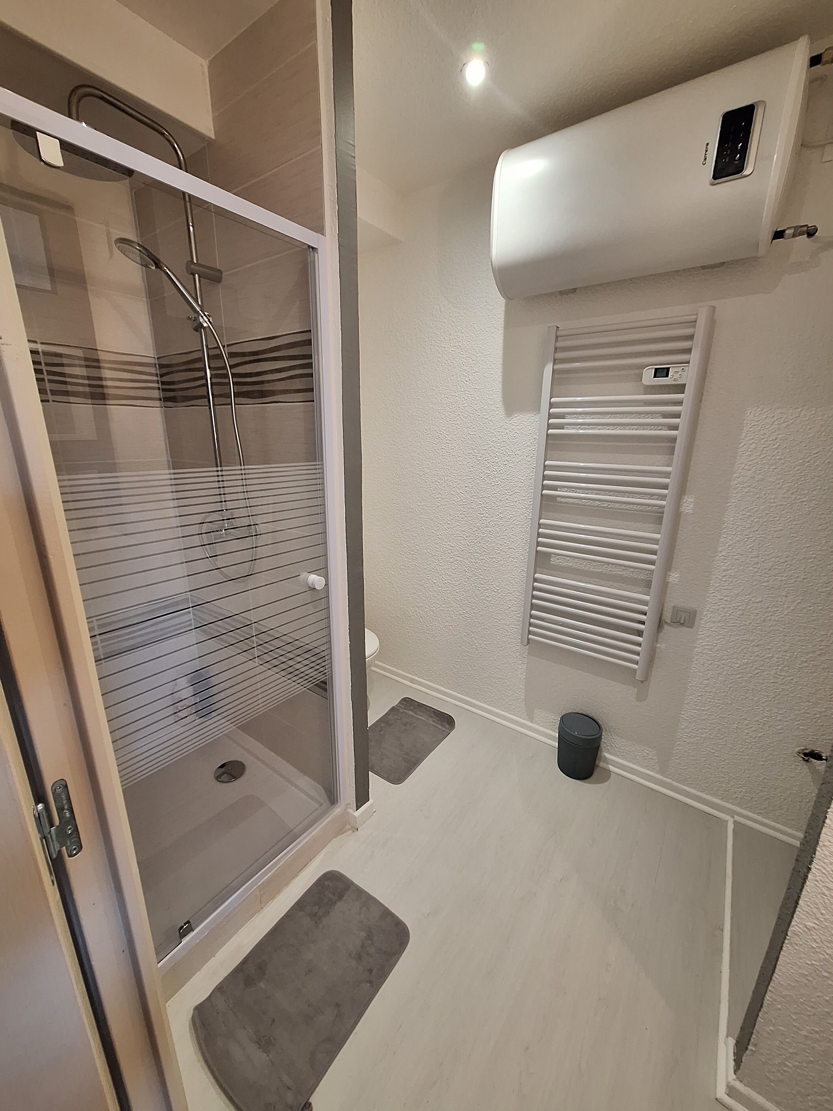 Ein modernes Badezimmer mit Duschkabine aus Glas, Toilette, Handtuchhalter und wandmontierter Klimaanlage.