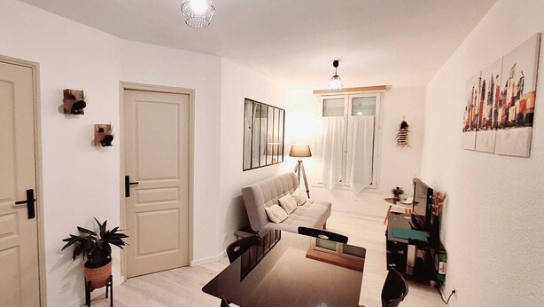 A living room with a sofa, a coffee table, a TV, a lamp, and a painting on the wall. - Attractive, renovated 2-room apartment by the lake (Saint-Jean-d'Angély)
