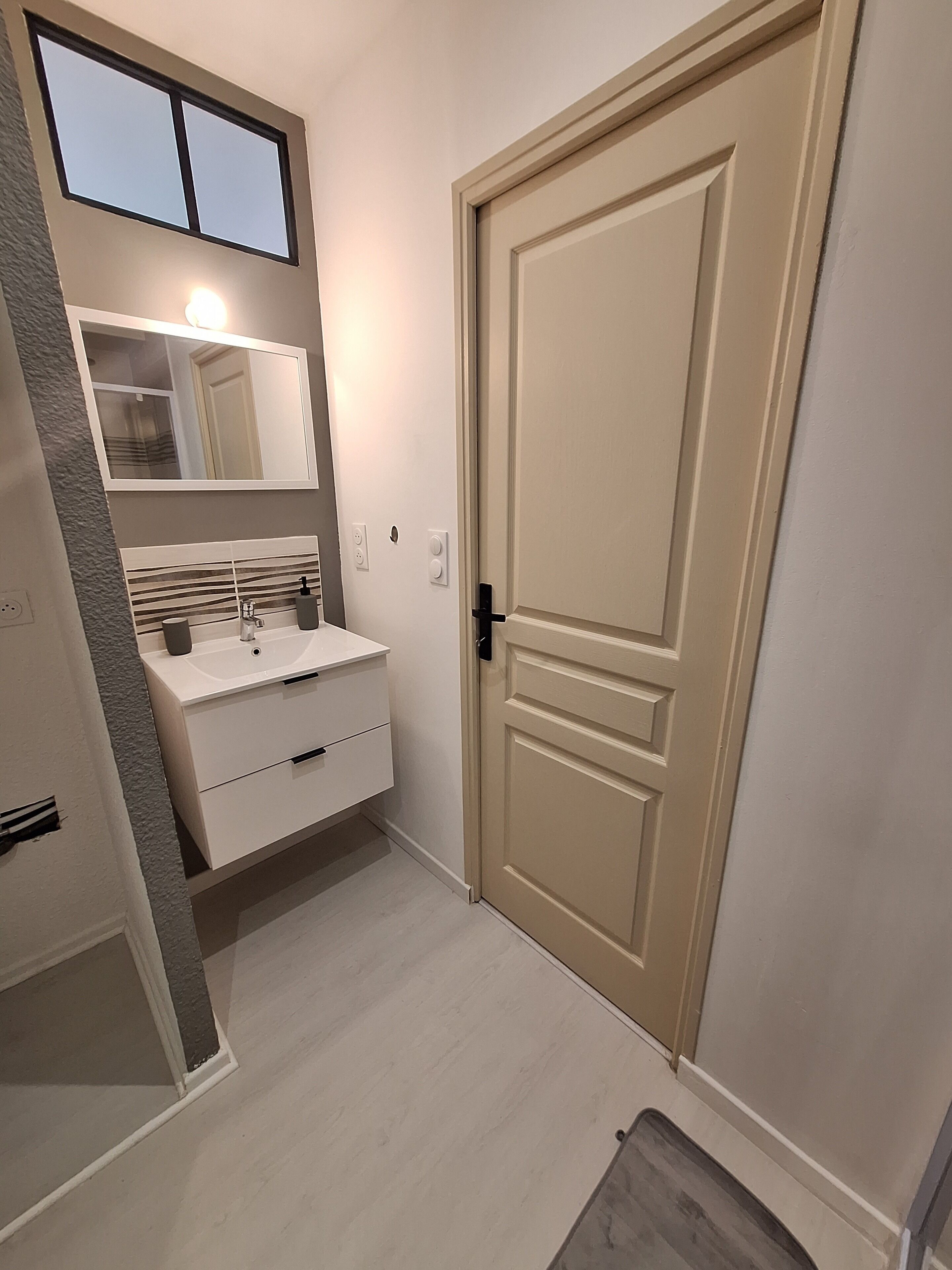 Un baño con lavamanos, espejo y puerta blancos.