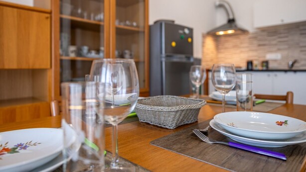 Une table à manger dressée avec des assiettes, des verres et un panier, dans une cuisine dotée de meubles en bois et d’un appareil électroménager moderne.