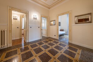 Un pasillo con piso estampado, puertas que dan a otras habitaciones y un espejo en la pared.