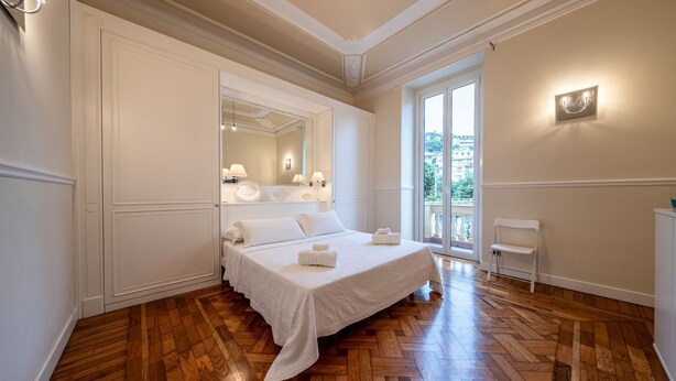 Un dormitorio con cama, espejo, lámparas de noche, una silla y vistas al exterior.