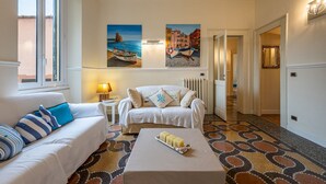 Habitación de hotel con sofá, una mesa de centro con una bandeja de objetos, una lámpara y dos cuadros en la pared.