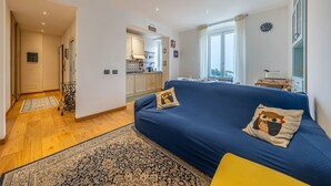 Un salon chaleureux avec un canapé bleu, un tapis à motifs et une vue sur la cuisine et le balcon.