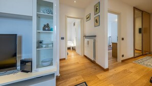 Un couloir avec un téléviseur, des étagères ornées d’objets décoratifs, un radiateur et une porte donnant sur une autre pièce.