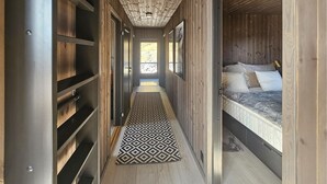 Un pasillo estrecho con una alfombra estampada, paredes de madera y una cama con almohadas.