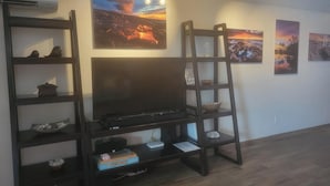 Un salon avec un téléviseur posé sur un meuble en bois, entouré d’étagères ornées d’objets décoratifs et de tableaux encadrés accrochés au mur.