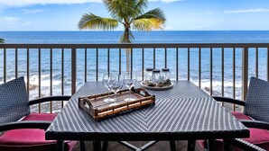 Un balcon avec une table dressée pour deux personnes, donnant sur l’océan, avec un palmier en arrière-plan.