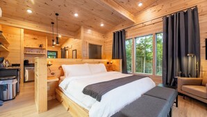 Une cabane en bois avec un grand lit, une petite kitchenette et une fenêtre avec des rideaux.