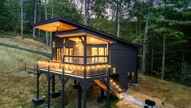 Une cabane en bois à deux étages, dotée d’un balcon et entourée d’arbres.