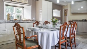 Zona de dinar amb una taula rodona preparada per a sis persones, envoltada de cadires de fusta amb seients mullidors.