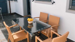 A dining area with a glass table and wicker chairs, a basket of lemons, and a white wall with shutters. - Viareggio House Renovated July 2024 (Viareggio)