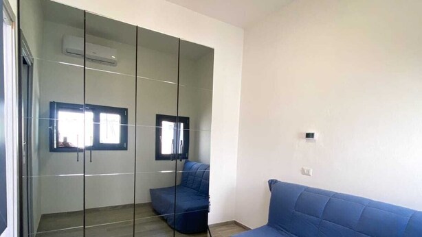 A modern room with a sliding glass door leading to a balcony, a blue sofa, and a flat-screen TV mounted on the wall. - Viareggio House Renovated July 2024 (Viareggio)