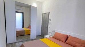 A bedroom with a bed, a bedside table, a mirror, and a wardrobe. - Viareggio House Renovated July 2024 (Viareggio)
