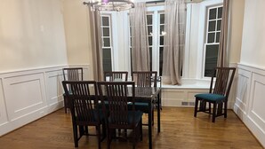 Un comedor con mesa y sillas de madera, una ventana con cortinas y vistas al exterior.
