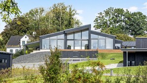 Ein modernes Haus mit großen Fenstern, einer Holzterrasse und einem Kiesweg.