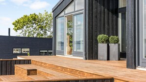 Ein modernes Gebäude mit großen Fenstern, einer Holzterrasse und zwei Kübelpflanzen.