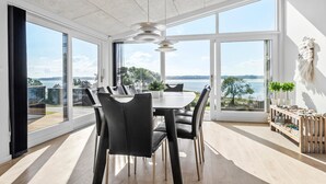 Ein moderner Essbereich mit einem großen Tisch und Stühlen, großen Fenstern mit Blick auf das Wasser und einer dekorativen Wandgestaltung.