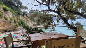 Una mesa y sillas de madera con vista a una playa y acantilados.