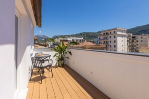 A balcony with a table and chairs, a potted plant, and a view of buildings and hills.
